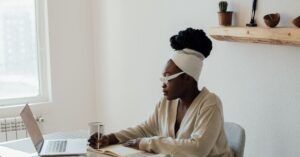 A focused woman is working independently with a laptop and notebook at her desk, illustrating the Manager of One mindset