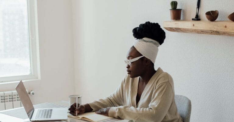A focused woman is working independently with a laptop and notebook at her desk, illustrating the Manager of One mindset