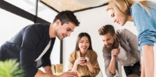 A group of four young professionals collaborating around a table, with one person leading the discussion. Optimized for the keyword 'how to lead your peers.