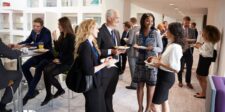 Professionals networking and socializing at a business event, holding plates with refreshments and engaging in conversations, illustrating a typical business networking event setting.