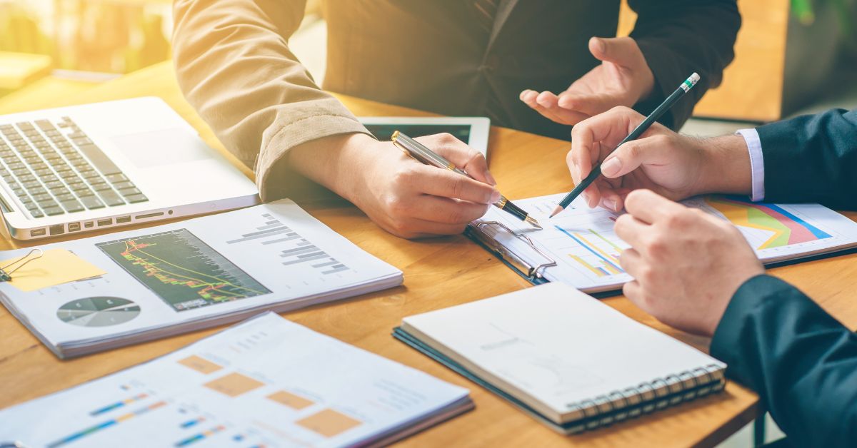 Two business professionals discussing charts and graphs on a table with a laptop, illustrating collaboration on how to write a business plan.