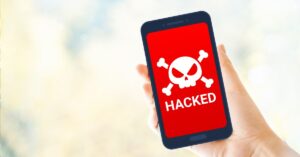 A hand holding a smartphone displaying a red warning screen with a skull and crossbones icon and the word "HACKED" in bold white letters, symbolizing a compromised Instagram account.