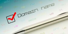 A metallic pen resting below the text 'Domain name' with a red checkmark in a checkbox, surrounded by colorful domain extensions like .com, .edu, and .us, symbolizing domain registration.