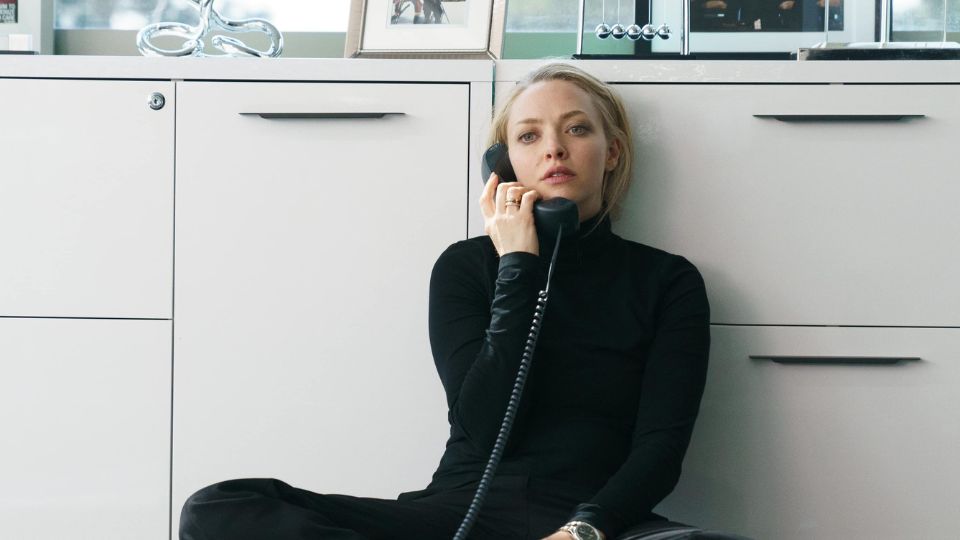 Promotional image for The Dropout showing a woman in black sitting on the floor of an office while holding a corded phone.
