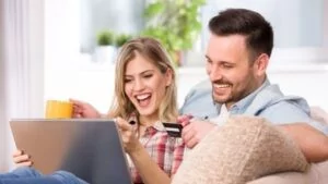 A smiling couple sitting on a couch using a laptop together, holding a credit card—representing satisfaction and success with persuasive digital content.
