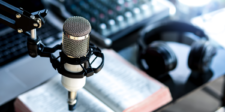 A podcast recording setup featuring a professional microphone on a stand, headphones, an open book, and audio equipment in the background.