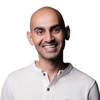 A bald man smiling, wearing a white button-up shirt against a white background.