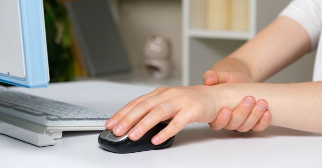 A person holding their wrist while using a computer mouse, suggesting discomfort or ergonomics in a workspace setting.