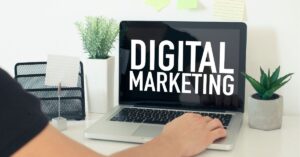 A person using a laptop displaying the words "DIGITAL MARKETING," with plants and office supplies on the desk. | digital marketing experts