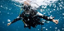 Scuba diver underwater, wearing diving gear and surrounded by bubbles.