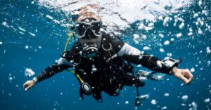 Scuba diver underwater, wearing diving gear and surrounded by bubbles.