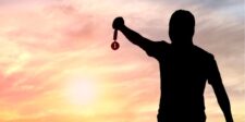 A man raises a key above his head against a vibrant sunset backdrop, symbolizing hope and new beginnings.