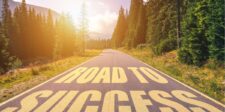 Sunny road through a forest with the words "ROAD TO SUCCESS" painted in large letters on the asphalt.