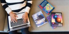 "Person using a laptop, surrounded by books on Java, compiler design, and computing fundamentals."