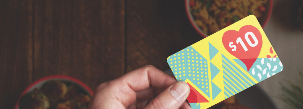 Hand holding a colorful $10 gift card with geometric patterns.