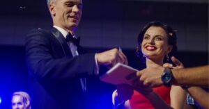 Two people in formal attire signing autographs at an event, with a crowd around them.