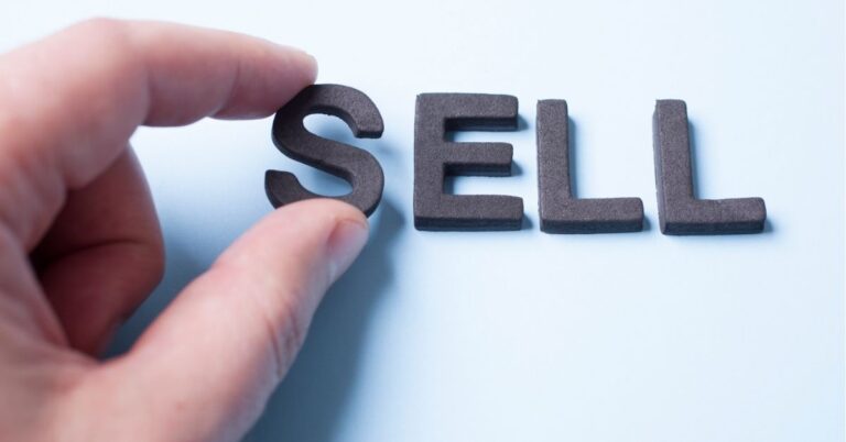 "Hand arranging letters to spell 'SELL' on a light background."