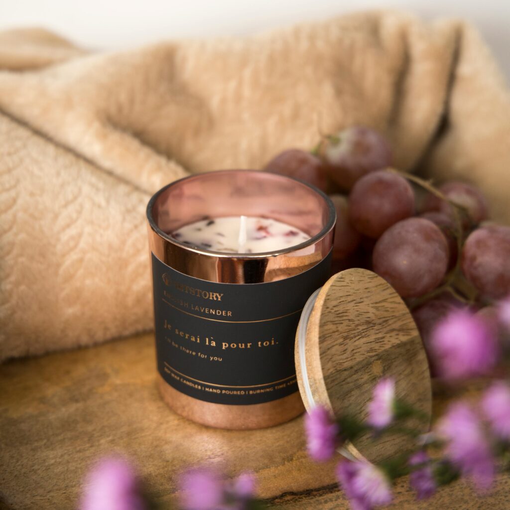 Luxury lavender candle on a wooden tray with grapes and a cozy blanket.