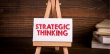 Small canvas on an easel with the words "STRATEGIC THINKING" in bold red text, set against a wooden background with books stacked on the side.