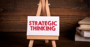 Small canvas on an easel with the words "STRATEGIC THINKING" in bold red text, set against a wooden background with books stacked on the side.