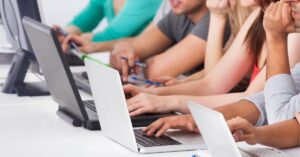 Group of people using laptops in a classroom setting.