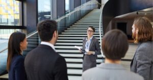 Business meeting by stairs, featuring a woman presenting to colleagues.