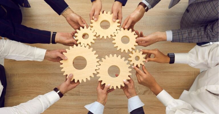 Hands holding interlocking wooden gears, symbolizing teamwork.
