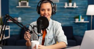 Person smiling while recording a podcast with a microphone and headphones.