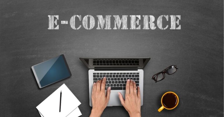Hands typing on a laptop with "E-COMMERCE" text above. Tablet, notepad, glasses, and coffee nearby.