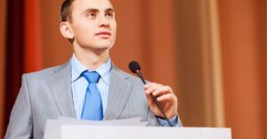 Person in a suit speaking at a podium with a microphone.