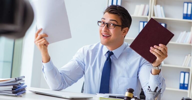 Professional man at a desk holding a book and documents, smiling.