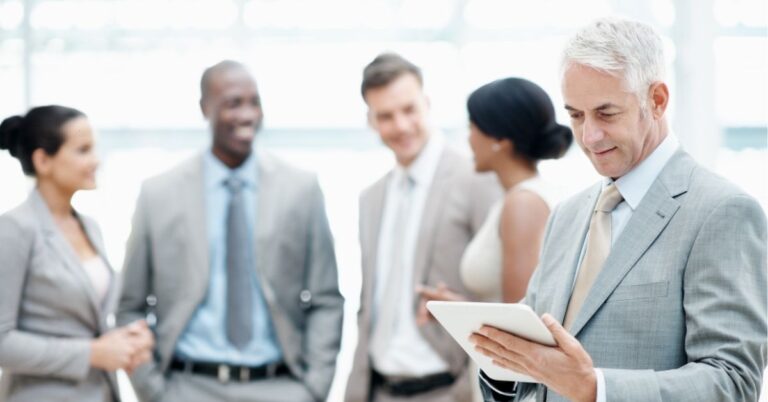 Business team in formal attire, with a man using a tablet in the foreground.