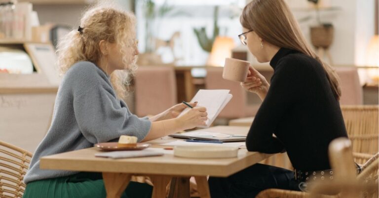 Two women collaborating over documents in a cozy cafe setting.