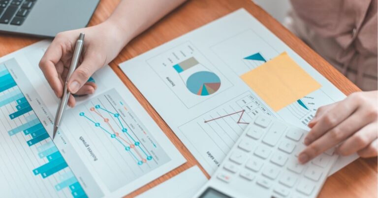 Person analyzing charts and graphs with a calculator and pen.