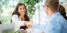 Smiling woman in a business meeting, shaking hands with a colleague across the table.