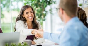 Smiling woman in a business meeting, shaking hands with a colleague across the table.