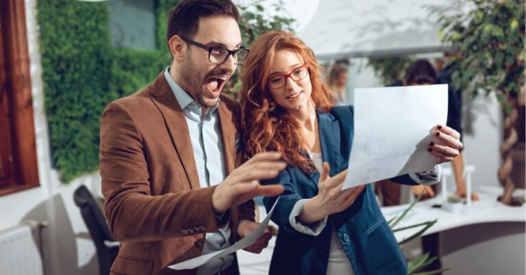 Two colleagues excitedly reviewing documents together in an office setting.