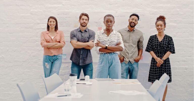 Team of five standing confidently in front of a whiteboard with notes and diagrams.