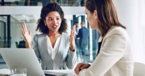 Two professionals in a business discussion at a desk with a laptop.