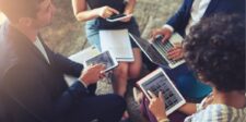 Professionals using tablets and a laptop in a collaborative meeting.