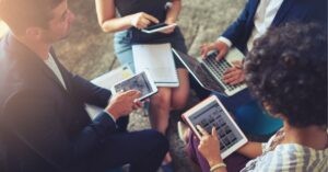 Professionals using tablets and a laptop in a collaborative meeting.