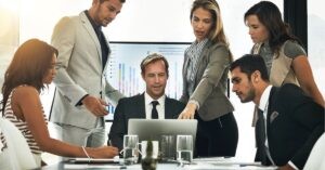 Group of professionals collaborating around a laptop with charts in the background.