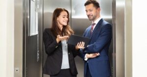 Two professionals in an elevator discussing on a tablet.