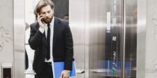 How To Control Your Elevator Pitch (Tips That Work) Man in a suit talking on the phone while exiting an elevator.