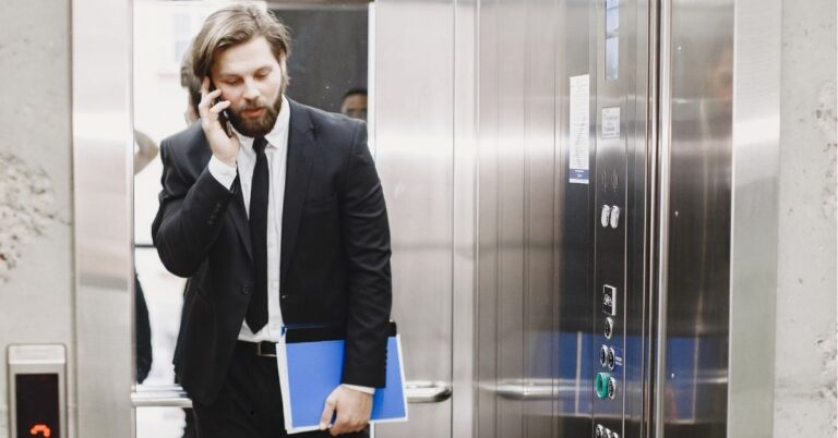 Man in a suit talking on the phone while exiting an elevator.