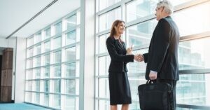 Two business professionals shaking hands in a modern office setting.
