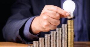 Hand placing a light bulb on stacked coins, symbolizing investment and ideas.