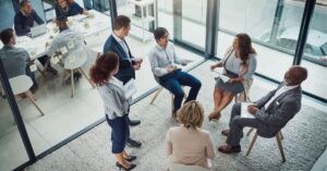 Group of professionals in a meeting, discussing around a table with notes and laptops.