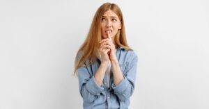 Thoughtful young woman with long red hair in a denim shirt, looking uncertain and biting her finger while thinking. The image illustrates how using thinking models can help prevent emotional chaos.
