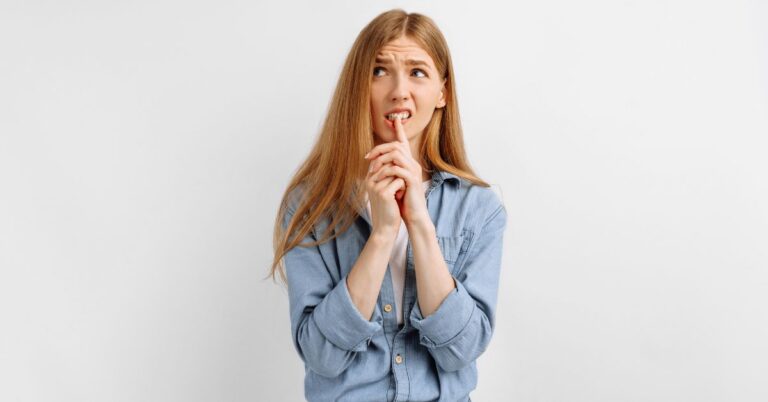 Thoughtful young woman with long red hair in a denim shirt, looking uncertain and biting her finger while thinking. The image illustrates how using thinking models can help prevent emotional chaos.